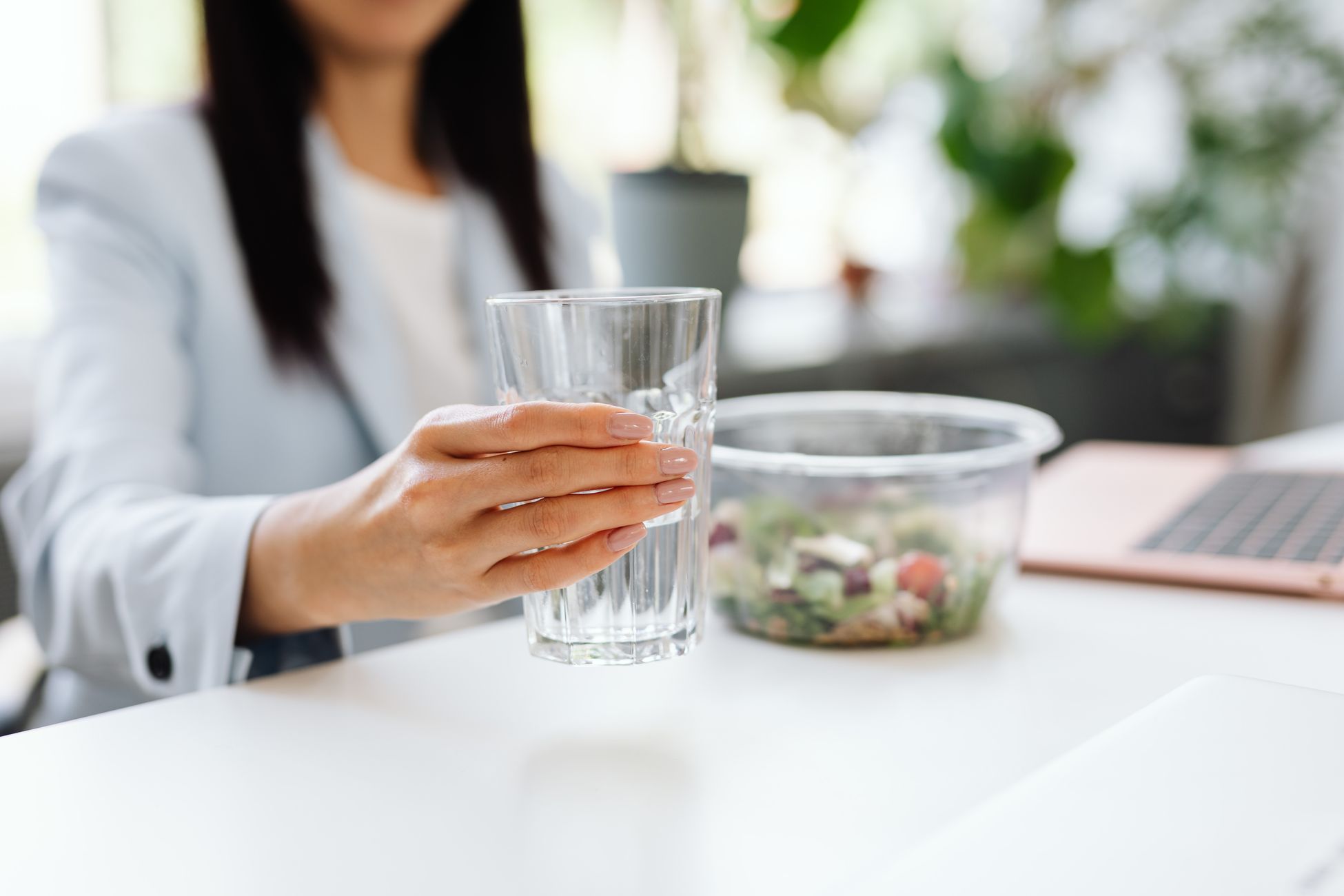 女性在办公桌前饮用杯中的水